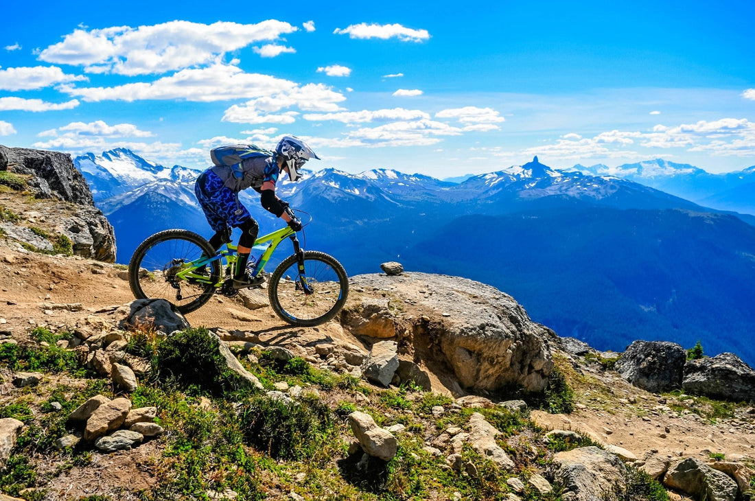 Mountain biker riding on a mountain with blue sky and mountains in background.