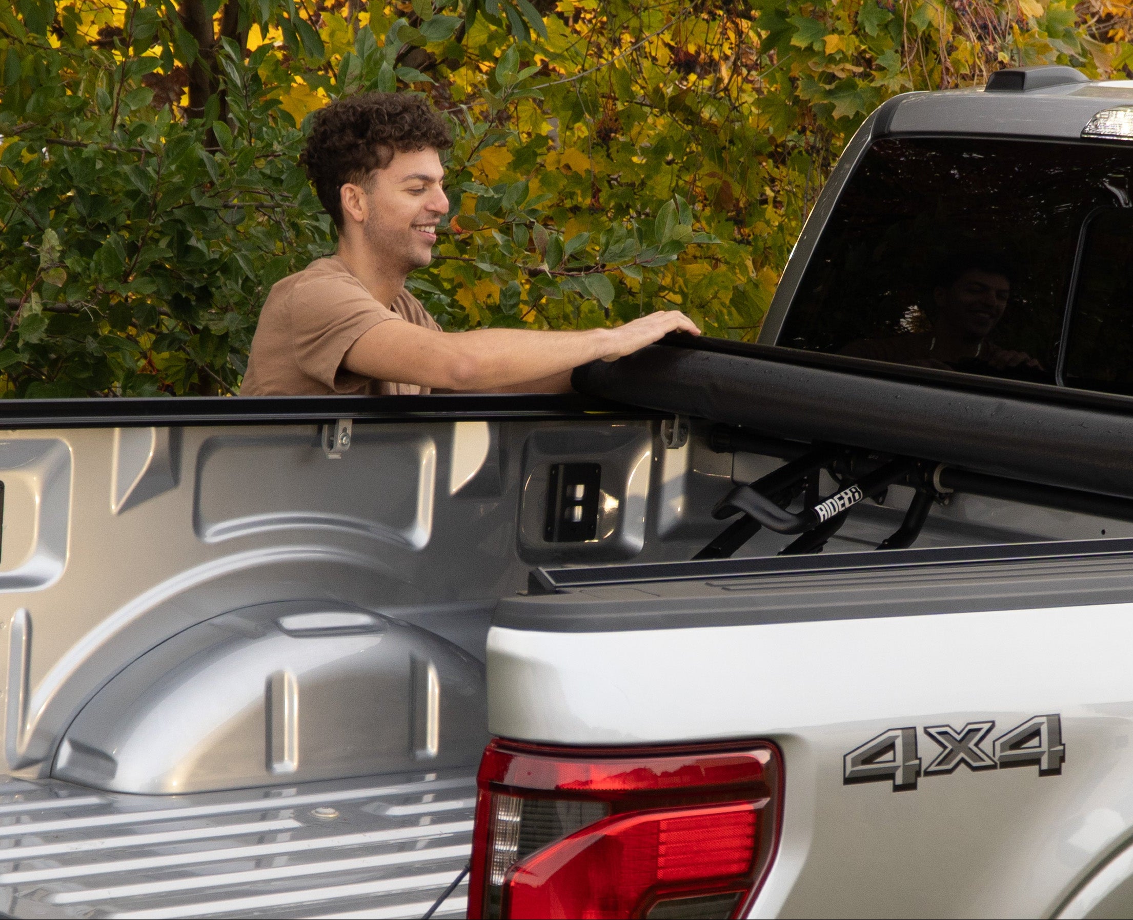 Man closing a tonneau cover over a truck bed with QR3 bike racks in their lowered position.