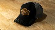 RIDE88 black and gray curved bill trucker hat with brown leather patch logo reading “RIDE88 Ultimate Truck Bike Racks,” featuring mesh back and contrast stitching.