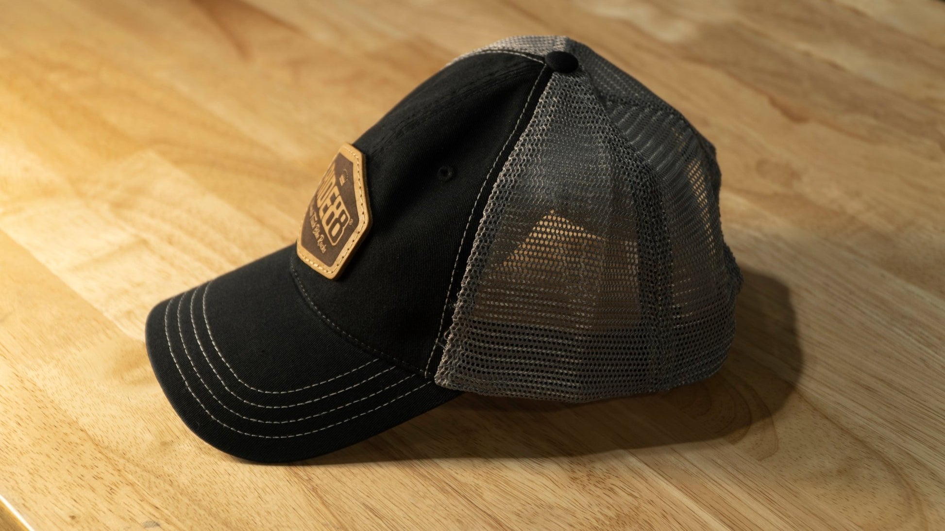 RIDE88 black and gray curved bill trucker hat with brown leather patch logo reading “RIDE88 Ultimate Truck Bike Racks,” featuring mesh back and contrast stitching.