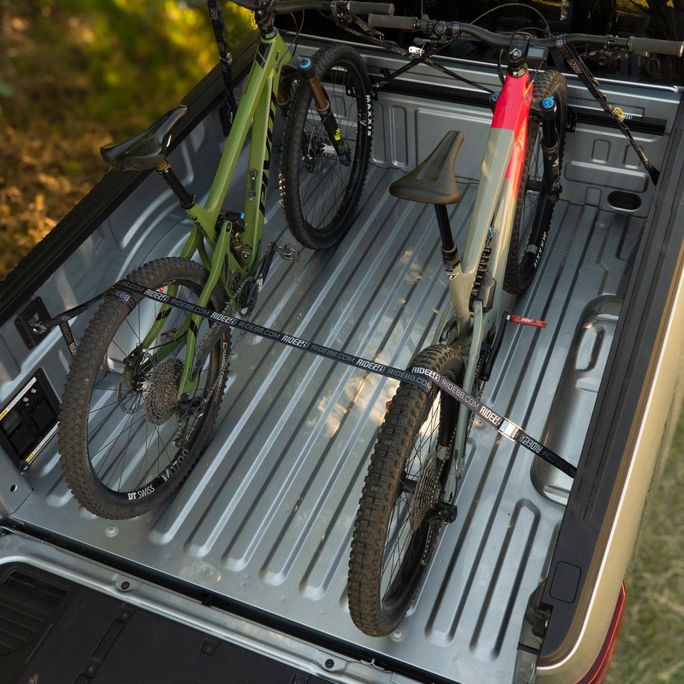 Two bikes mounted to the bed of a truck using a RIDE88 U-Track Cinch Rack. The rear tires of the bikes are also held down by a Rear Strap Tie-Down.