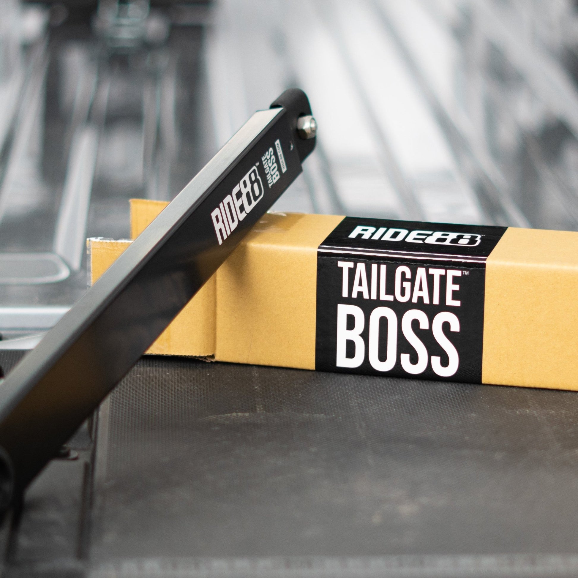 RIDE88 Tailgate Boss tailgate support resting on cardboard box with black sticker with white text that says "RIDE88 TAILGATE BOSS".