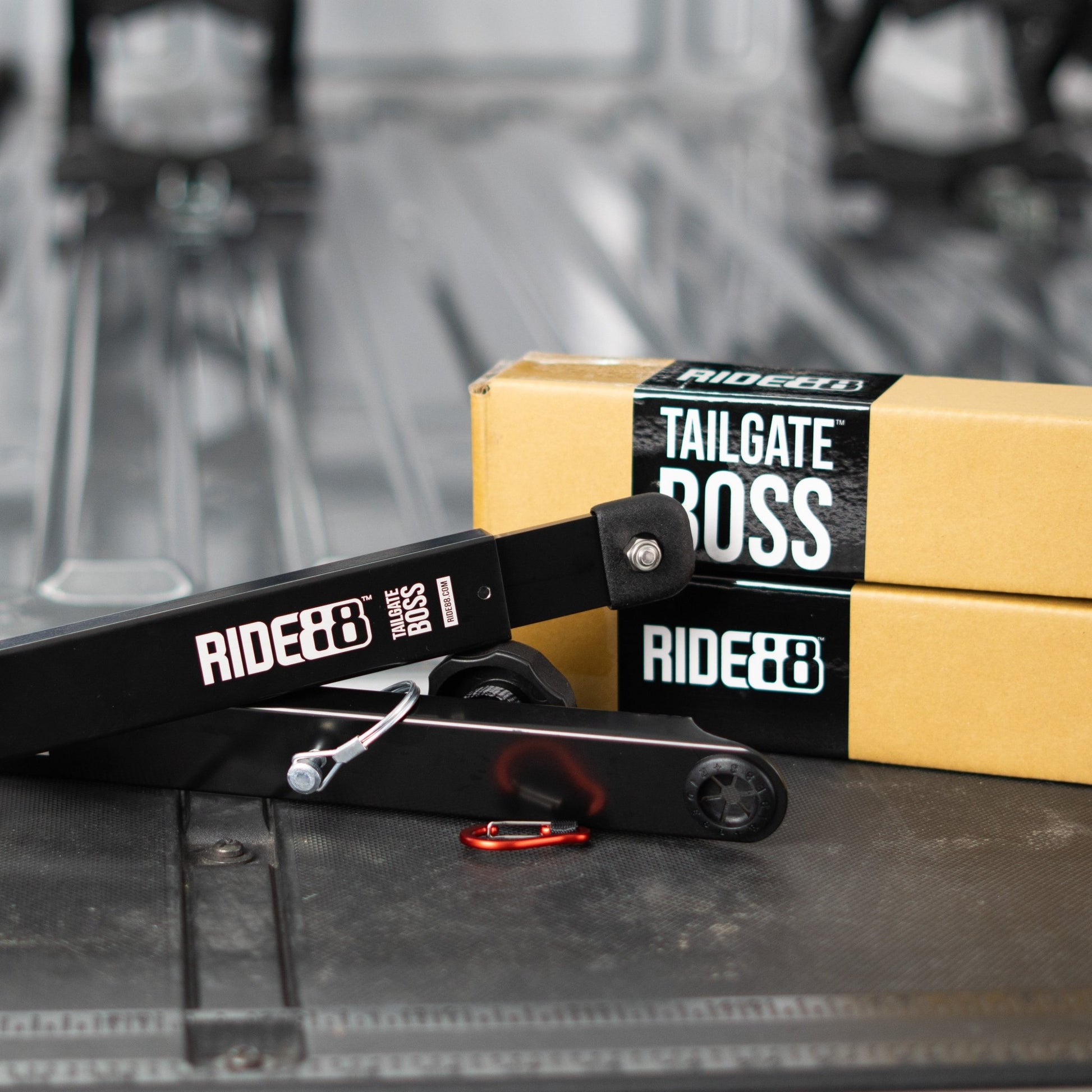RIDE88 Tailgate Boss Pro-Kit tailgate support bars resting in front of cardboard boxes with black stickers with white text that says "RIDE88 TAILGATE BOSS".
