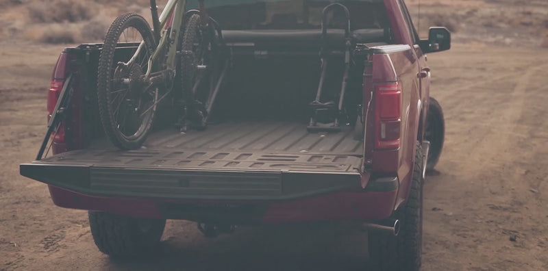 Rider loading a mountain bike into a RIDE88 QR3 Truck Bed Bike Rack mounted in a pickup truck.