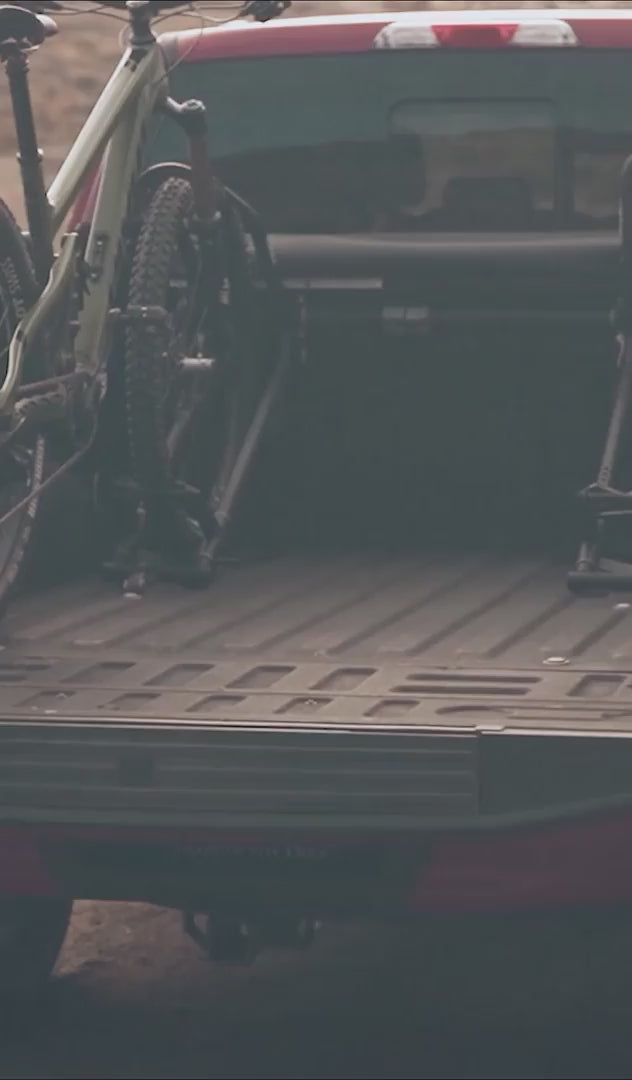 Rider loading a mountain bike into a RIDE88 QR3 Truck Bed Bike Rack mounted in a pickup truck.